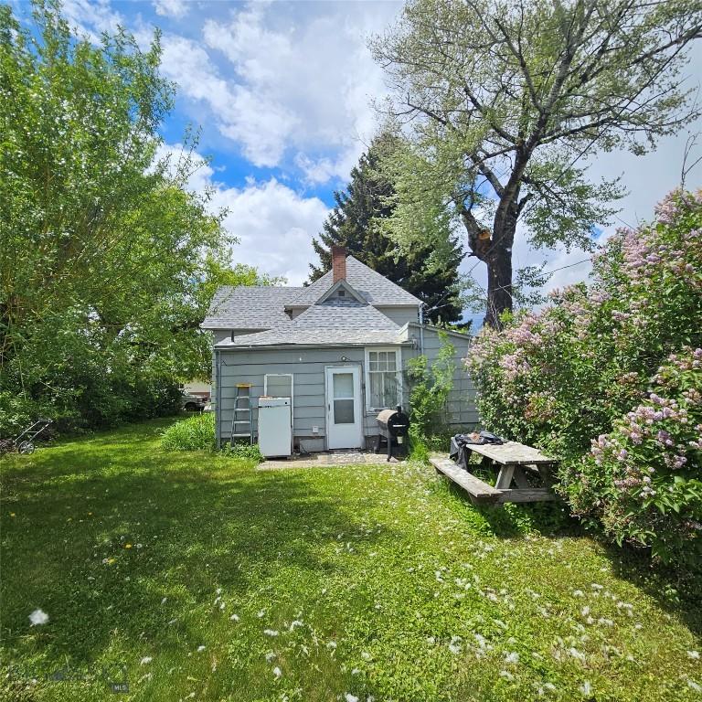 214 N Cedar St, Townsend, MT 59644 - back of house featuring a yard, roof with shingles, a chimney, and an outbuilding