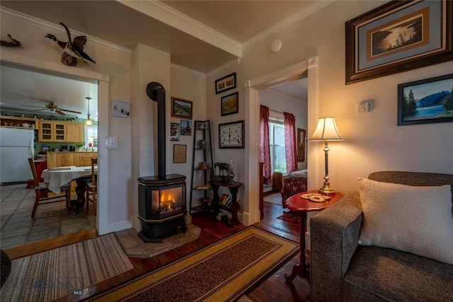 207 2nd St E, Clyde Park, MT 59018 - living room featuring a wood stove, ceiling fan, crown molding, wood finished floors, and baseboards