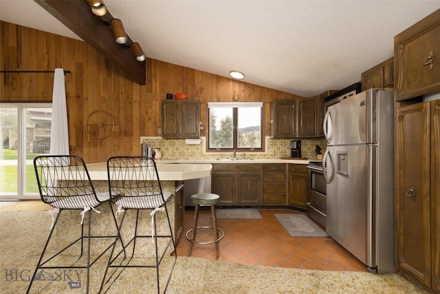 1930 Yellowtail, Big Sky, MT 59716 - kitchen with stainless steel appliances, lofted ceiling, light countertops, wood walls, and light tile patterned floors