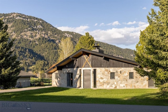 1930 Yellowtail, Big Sky, MT 59716 - view of side of home featuring stone siding, a mountain view, a chimney, and a yard