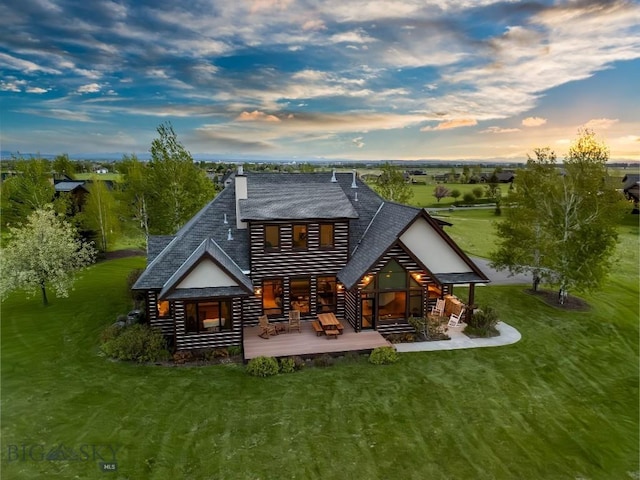 306 Glenbrook Ln, Belgrade, MT 59714 - back of house at dusk featuring a yard, a wooden deck, roof with shingles, log veneer siding, and a chimney