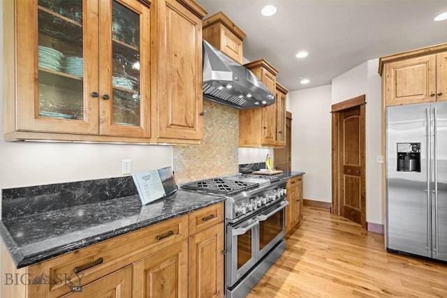 306 Glenbrook Ln, Belgrade, MT 59714 - kitchen featuring appliances with stainless steel finishes, wall chimney range hood, light wood-style floors, dark stone counters, and tasteful backsplash