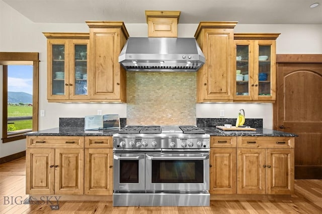 306 Glenbrook Ln, Belgrade, MT 59714 - kitchen with double oven range, wall chimney range hood, light wood-type flooring, dark stone counters, and glass insert cabinets