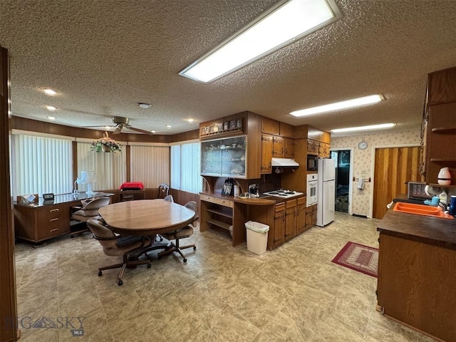 2301 Banks Ave, Butte, MT 59701 - kitchen featuring a textured ceiling, white appliances, under cabinet range hood, dark countertops, and brown cabinetry
