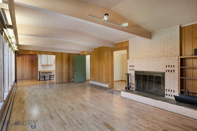 1524 S Grand, Bozeman, MT 59715 - unfurnished living room featuring a baseboard heating unit, wooden walls, wood finished floors, a fireplace, and a textured ceiling