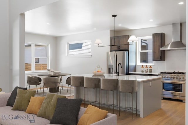 4149 Annie St, Bozeman, MT 59718 - kitchen featuring wall chimney exhaust hood, stainless steel appliances, a sink, light wood-type flooring, and an island with sink