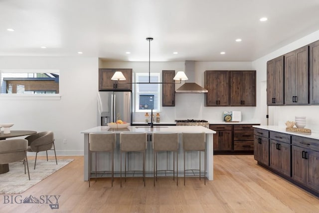4149 Annie St, Bozeman, MT 59718 - kitchen featuring stainless steel refrigerator with ice dispenser, wall chimney exhaust hood, dark brown cabinetry, a kitchen breakfast bar, and a center island with sink