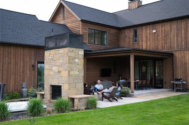 529 Clancy Way, Bozeman, MT 59718 - rear view of house with an outdoor stone fireplace, a patio area, roof with shingles, a chimney, and a lawn