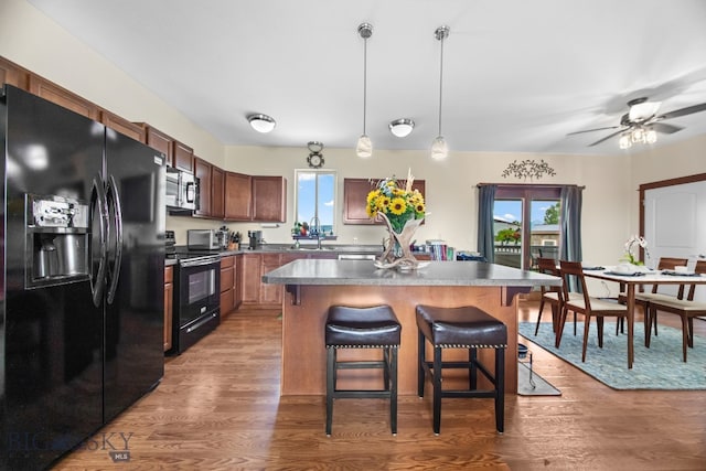 191 Barnes Dr, Belgrade, MT 59714 - kitchen featuring black appliances, a breakfast bar area, light wood-style flooring, decorative light fixtures, and a kitchen island