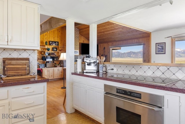 25 Trail Creek Rd, Ennis, MT 59729 - kitchen featuring stainless steel oven, dark countertops, wood walls, and white cabinets