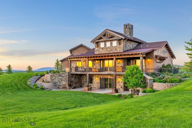 715 Bates Rd, Manhattan, MT 59741 - back of property at dusk with stone siding, a patio, and a lawn