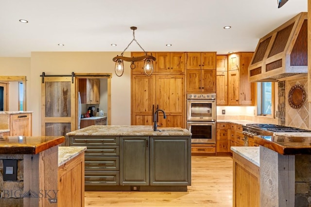 715 Bates Rd, Manhattan, MT 59741 - kitchen with appliances with stainless steel finishes, light wood-style floors, custom exhaust hood, an island with sink, and recessed lighting