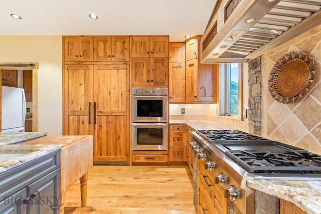 715 Bates Rd, Manhattan, MT 59741 - kitchen featuring appliances with stainless steel finishes, custom range hood, light wood-type flooring, light stone counters, and recessed lighting