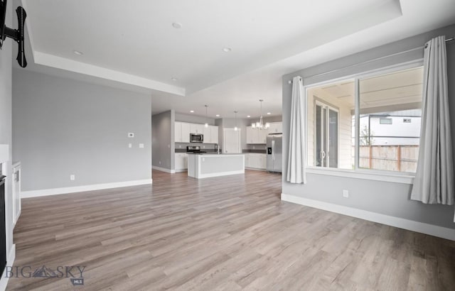 1518 Deadwood Loop, Belgrade, MT 59714 - unfurnished living room featuring baseboards, light wood-type flooring, recessed lighting, a chandelier, and a tray ceiling