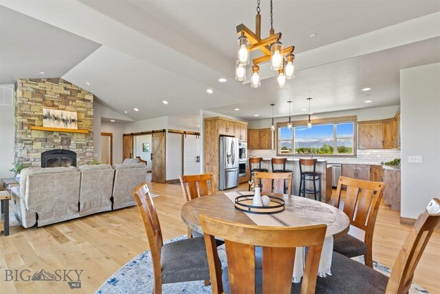 3483 Highline Rd, Manhattan, MT 59741 - dining room featuring light wood-type flooring, a fireplace, vaulted ceiling, recessed lighting, and a barn door