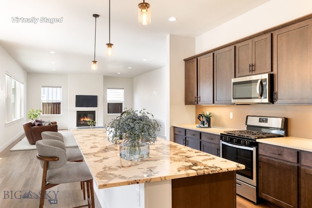 1609 Wyatt Earp Ct, Belgrade, MT 59714 - kitchen with appliances with stainless steel finishes, light wood-style floors, a glass covered fireplace, hanging light fixtures, and recessed lighting