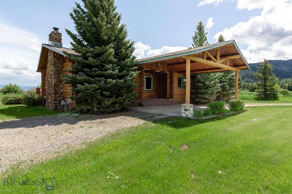 8212 War Eagle, Bozeman, MT 59718 - view of front of house with log siding, a chimney, a front lawn, and an attached carport