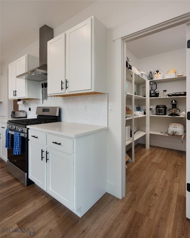 810 Butler Crk, Belgrade, MT 59714 - kitchen with gas range, wall chimney range hood, wood finished floors, light countertops, and white cabinets