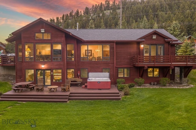 48042 Gallatin Rd, Big Sky, MT 59730 - back of property at dusk featuring a hot tub, a deck, a lawn, and roof with shingles