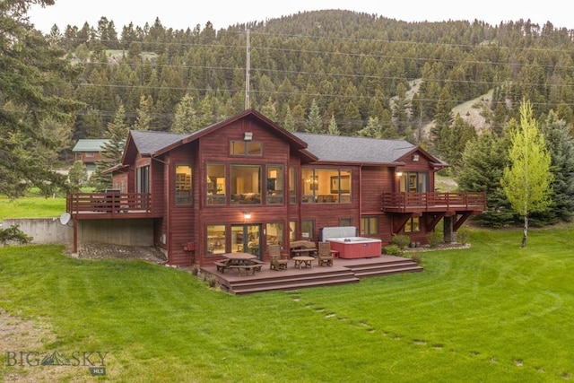 48042 Gallatin Rd, Big Sky, MT 59730 - rear view of property with a hot tub, a deck, a view of trees, and a lawn