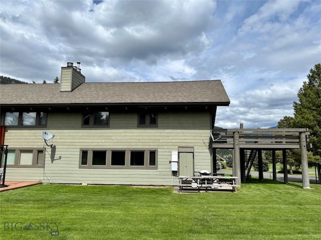 2225 Black Otter Rd Unit 23, Big Sky, MT 59716 - rear view of property featuring a yard, a chimney, a wooden deck, and a shingled roof