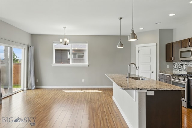 110 Ramshorn Peak Ln, Bozeman, MT 59718 - kitchen with stainless steel appliances, a sink, light wood-type flooring, an island with sink, and light stone counters