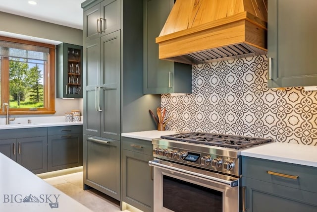 2594 Star Ridge Rd, Bozeman, MT 59715 - kitchen featuring stainless steel stove, custom range hood, light countertops, backsplash, and glass insert cabinets