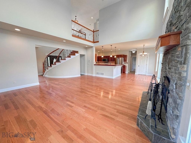 2475 Rose St, Bozeman, MT 59718 - unfurnished living room with a chandelier, light wood-style flooring, a high ceiling, a stone fireplace, and stairs