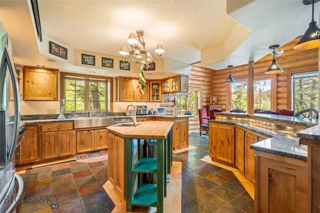 1561/1563 Colorado Gulch Dr, Helena, MT 59601 - kitchen featuring log walls, an island with sink, butcher block counters, brown cabinetry, and decorative light fixtures