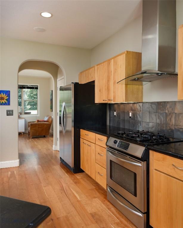 15 Blue Grouse Ct, Bozeman, MT 59715 - kitchen with wall chimney exhaust hood, appliances with stainless steel finishes, arched walkways, light wood finished floors, and recessed lighting