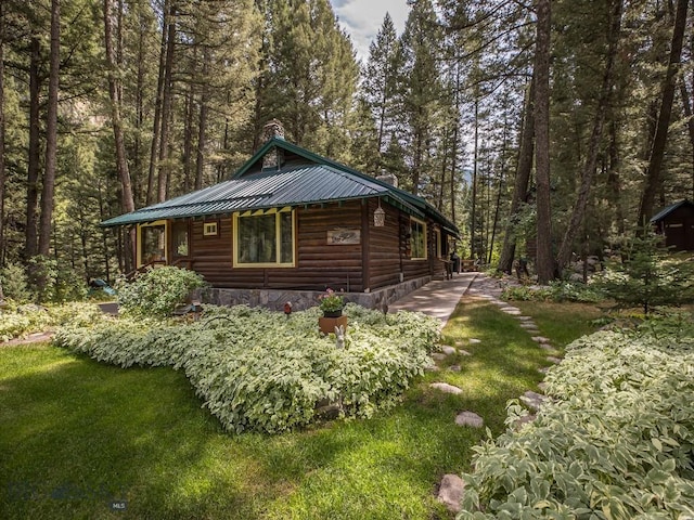 64370 Gallatin Rd, Gallatin Gateway, MT 59730 - view of side of home with log veneer siding, a chimney, a wooded view, a metal roof, and a yard