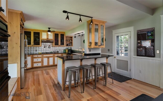 311 N 6th St, Manhattan, MT 59741 - kitchen with a peninsula, a ceiling fan, light wood-type flooring, dark countertops, and decorative backsplash