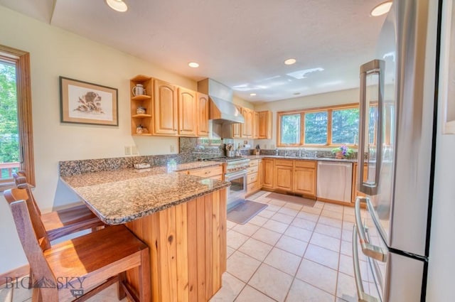 886 Wierda Way, Manhattan, MT 59741 - kitchen featuring wall chimney range hood, stainless steel appliances, light brown cabinets, a peninsula, and a breakfast bar area