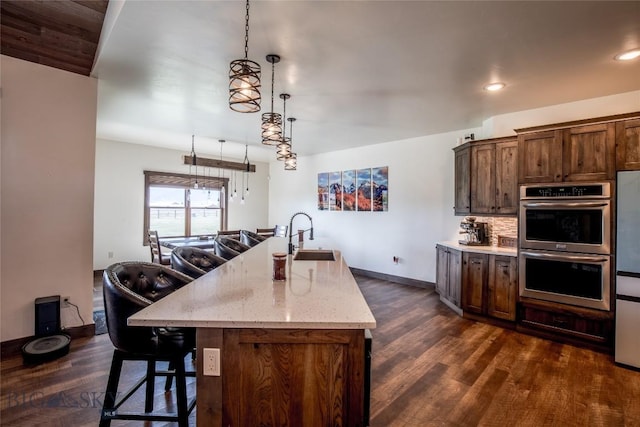 8 Sunset Ct, Ennis, MT 59729 - kitchen with dark wood-style flooring, stainless steel double oven, light stone countertops, an island with sink, and a breakfast bar area