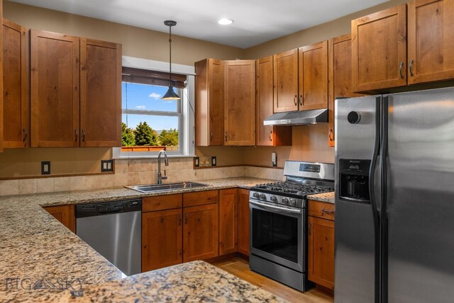 109 Baker St, Belgrade, MT 59714 - kitchen with appliances with stainless steel finishes, under cabinet range hood, light wood-style floors, light stone counters, and decorative light fixtures