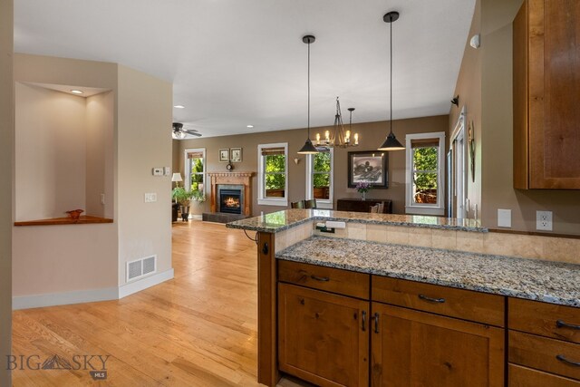 109 Baker St, Belgrade, MT 59714 - kitchen featuring a peninsula, a tile fireplace, brown cabinets, open floor plan, and light stone counters