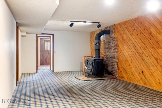 117 Henderson St, Bozeman, MT 59715 - unfurnished living room featuring wooden walls, carpet flooring, a wood stove, and a textured ceiling