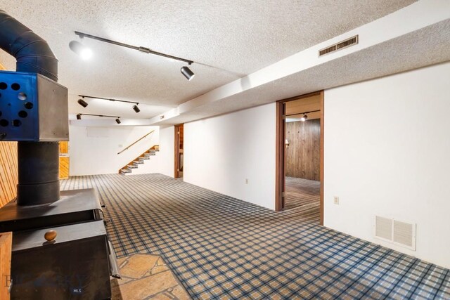 117 Henderson St, Bozeman, MT 59715 - finished basement featuring a wood stove, carpet floors, a textured ceiling, stairs, and track lighting