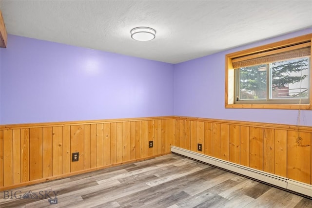 3573 Spain Bridge Rd, Belgrade, MT 59714 - spare room featuring baseboard heating, wainscoting, wood finished floors, wooden walls, and a textured ceiling