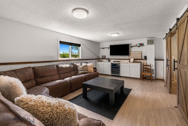 24151 Frontage Rd, Bozeman, MT 59718 - living room featuring a barn door, beverage cooler, light wood-type flooring, and a textured ceiling