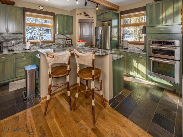 1255 Andesite Rd, Big Sky, MT 59716 - kitchen featuring green cabinets, appliances with stainless steel finishes, decorative backsplash, and light stone counters