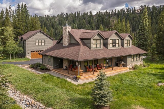 1255 Andesite Rd, Big Sky, MT 59716 - view of front of property with a wooded view, a chimney, a porch, and stone siding