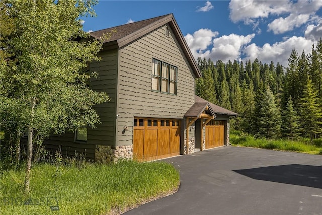 1255 Andesite Rd, Big Sky, MT 59716 - view of home's exterior with stone siding, asphalt driveway, a forest view, and a garage
