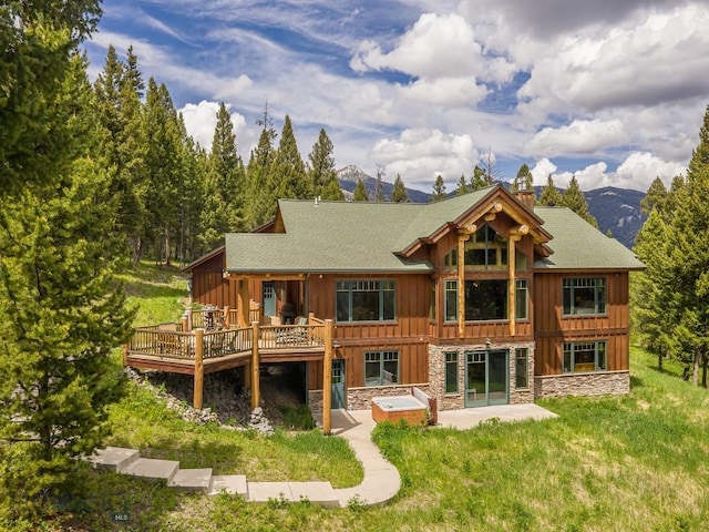 725 Sandhill Rd, Big Sky, MT 59716 - rear view of house with a patio, a deck with mountain view, board and batten siding, a chimney, and an outdoor hot tub