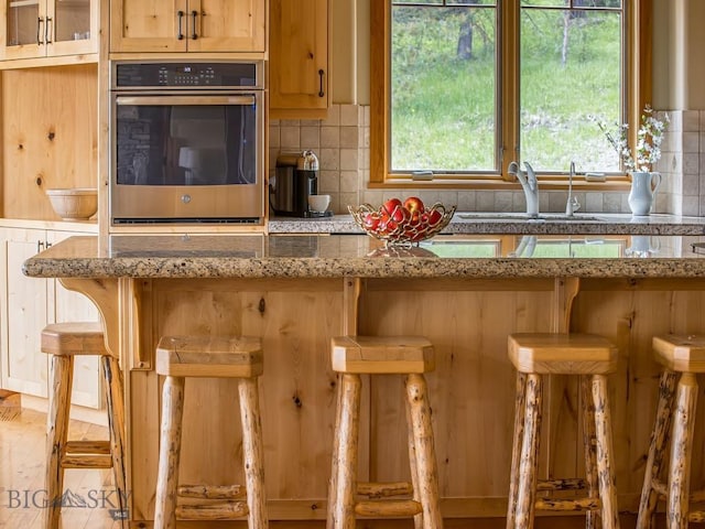 725 Sandhill Rd, Big Sky, MT 59716 - kitchen featuring stainless steel oven, backsplash, a kitchen bar, and light stone countertops