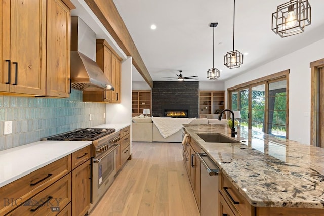 33 Leachman Ln, Bozeman, MT 59718 - kitchen with stainless steel appliances, wall chimney range hood, ceiling fan, a large fireplace, and light wood-type flooring