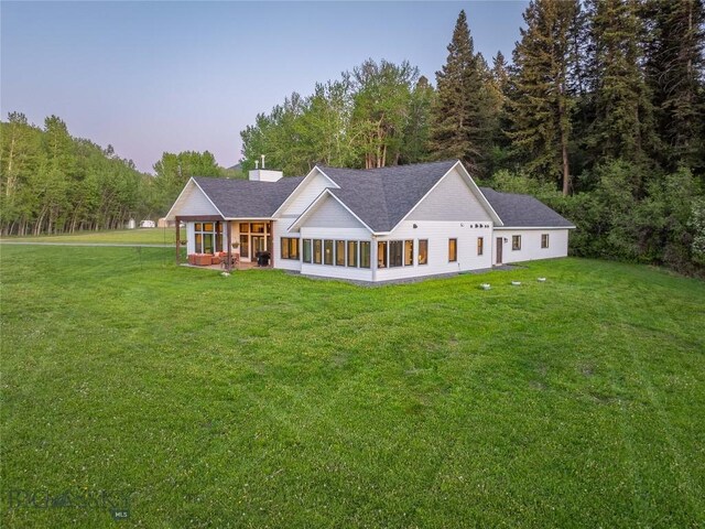 13011 Cottonwood Canyon Rd, Bozeman, MT 59718 - rear view of property featuring a sunroom, a lawn, a shingled roof, and a wooded view