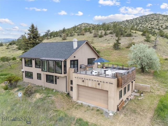 145 Spring Creek Hills Rd, Livingston, MT 59047 - rear view of house with a chimney, an attached garage, roof with shingles, dirt driveway, and a deck with mountain view