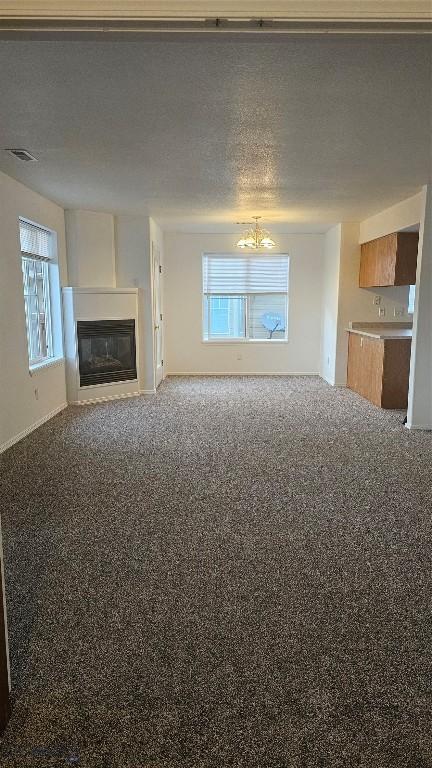 835 Forestglen Unit H, Bozeman, MT 59718 - unfurnished living room featuring a glass covered fireplace, healthy amount of natural light, a chandelier, carpet flooring, and a textured ceiling