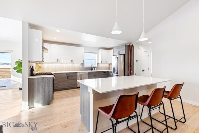 1991 Ryun Sun Way, Bozeman, MT 59718 - kitchen featuring appliances with stainless steel finishes, a breakfast bar area, light wood-style floors, backsplash, and light countertops